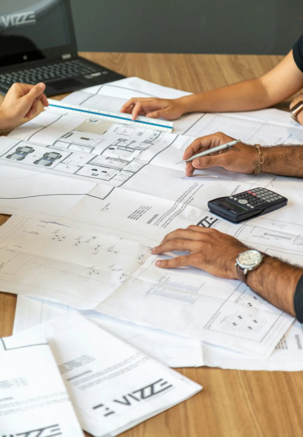 Des professionnels examinent des plans architecturaux à l’aide d’une calculatrice et d’un stylo.